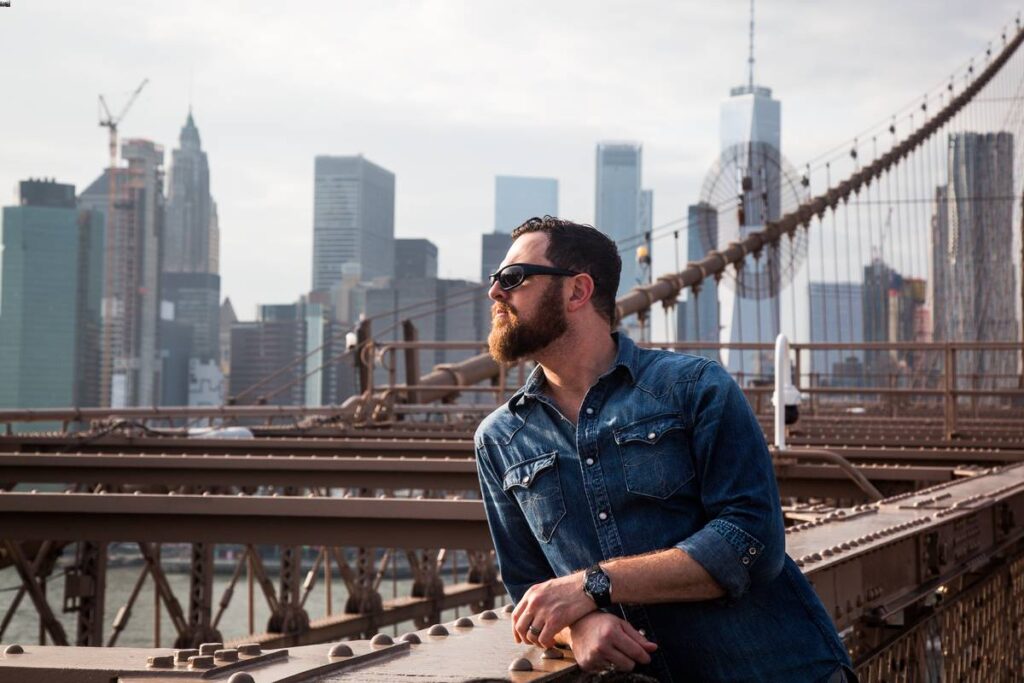 "What to wear in New York" hero image - a Stylish man on Brooklyn Bridge